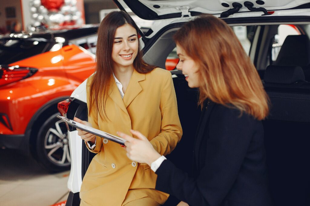 Two women reviewing paperwork for a car sale.